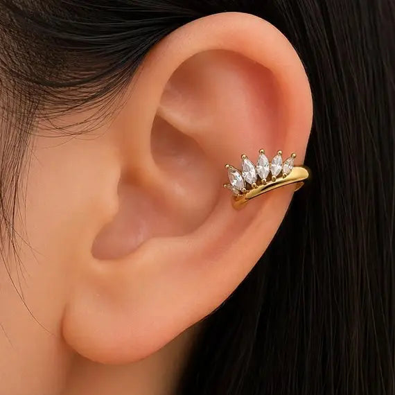 A close-up of a person's ear wearing a gold ear cuff adorned with small clear marquise-shaped stones.