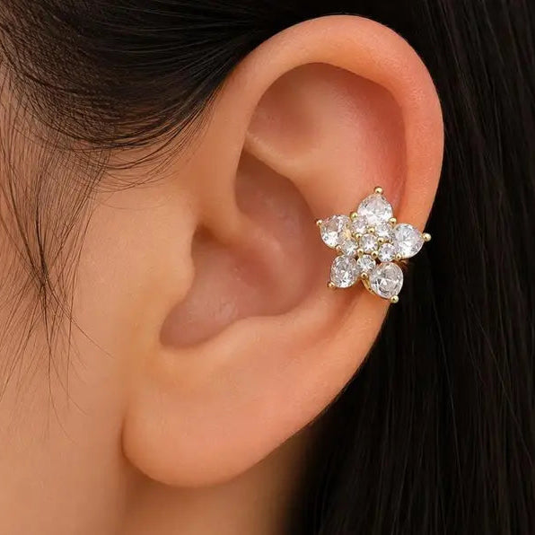A close-up of a person's ear wearing a gold flower-shaped ear cuff adorned with clear sparkling stones.