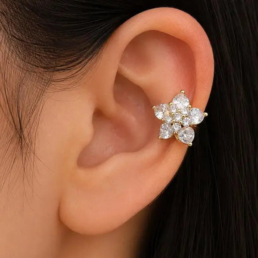 A close-up of a person's ear wearing a gold flower-shaped ear cuff adorned with clear sparkling stones.
